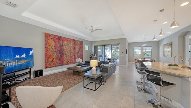 living room featuring a tray ceiling, ceiling fan, and sink