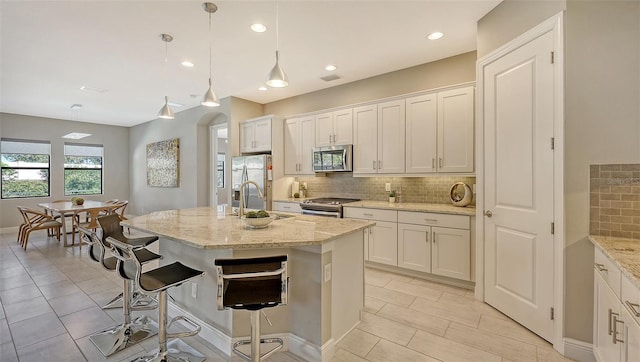 kitchen featuring decorative backsplash, a kitchen island with sink, stainless steel appliances, and light stone counters