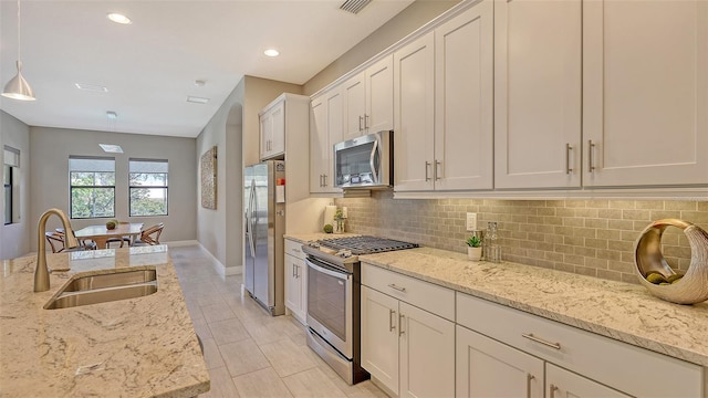 kitchen with light stone counters, sink, hanging light fixtures, and appliances with stainless steel finishes