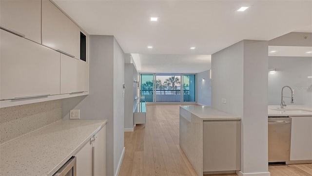 kitchen with expansive windows, sink, stainless steel dishwasher, light wood-type flooring, and light stone countertops