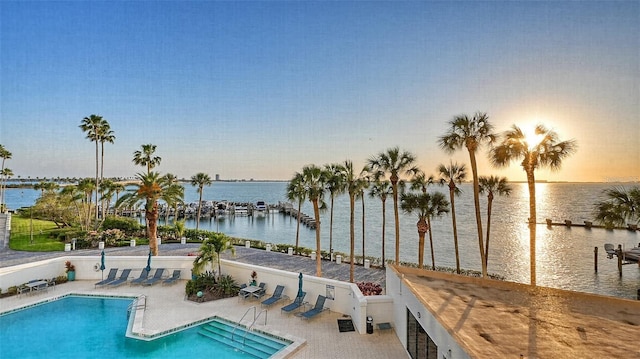 pool at dusk featuring a patio area and a water view