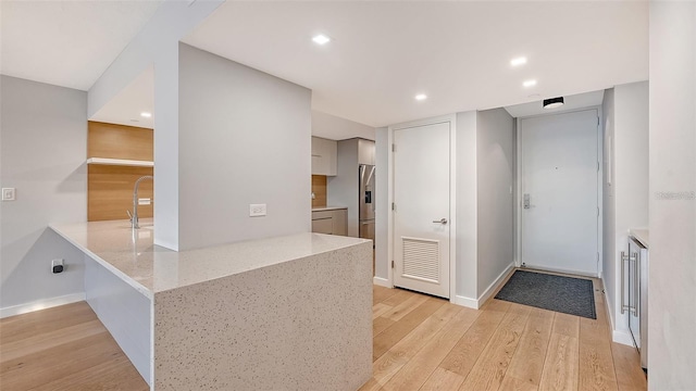 kitchen with kitchen peninsula, sink, light stone countertops, light hardwood / wood-style floors, and stainless steel fridge with ice dispenser