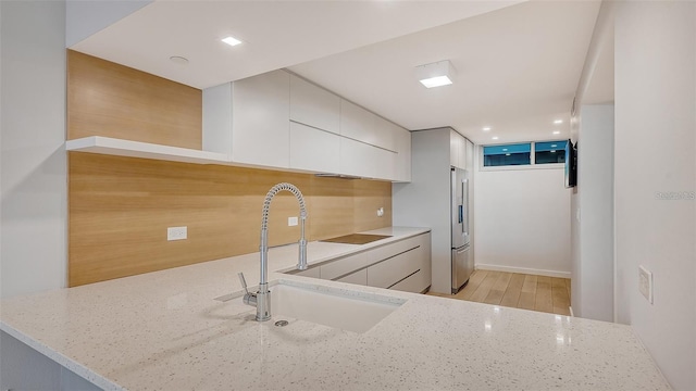 kitchen with white cabinets, sink, light hardwood / wood-style floors, high end fridge, and light stone counters