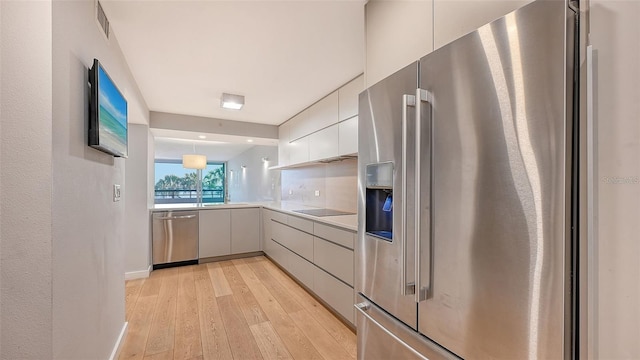 kitchen featuring white cabinetry, hanging light fixtures, stainless steel appliances, decorative backsplash, and light wood-type flooring