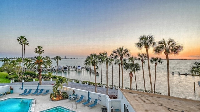 pool at dusk with a patio area and a water view