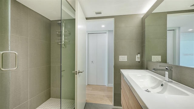 bathroom featuring a shower with door, vanity, and tile walls