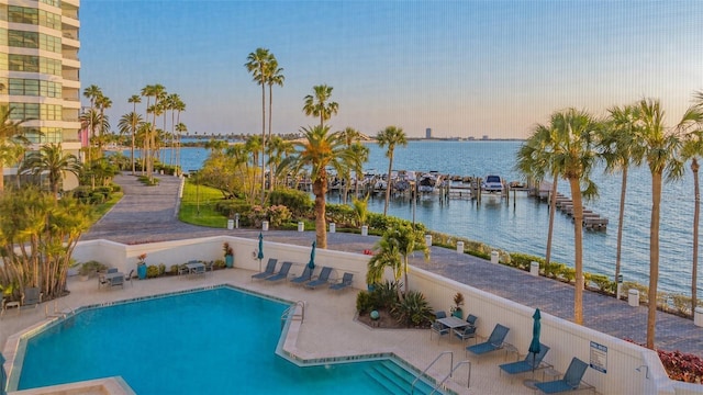 pool at dusk featuring a water view and a patio area