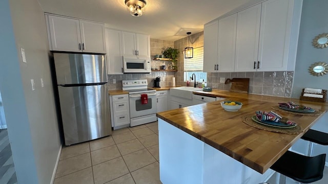 kitchen with butcher block counters, sink, kitchen peninsula, white appliances, and white cabinets