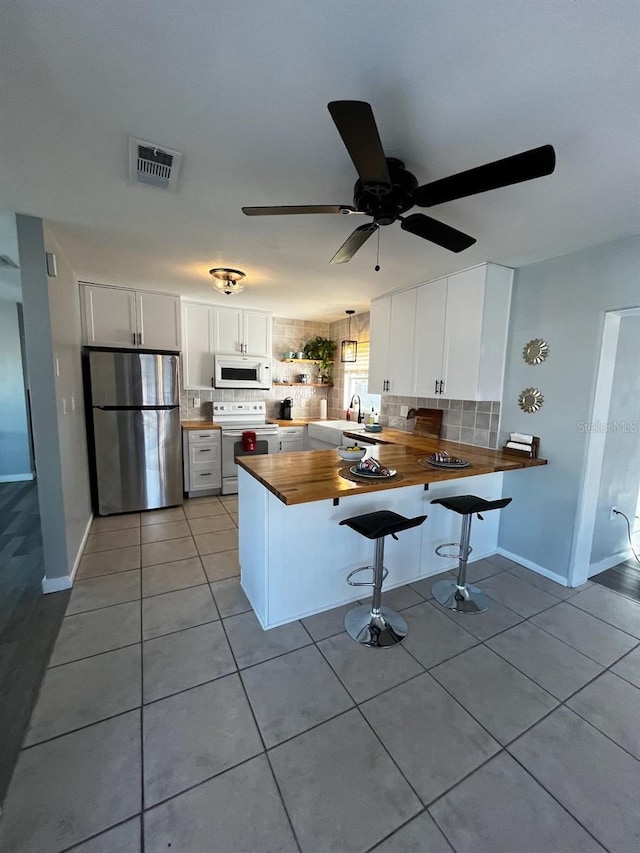 kitchen featuring butcher block counters, light tile patterned floors, kitchen peninsula, white appliances, and white cabinets