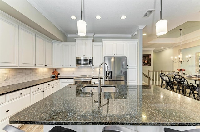 kitchen featuring a large island with sink, sink, dark stone counters, and appliances with stainless steel finishes