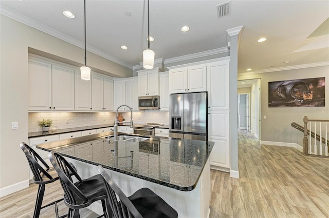 kitchen featuring white cabinetry, sink, stainless steel appliances, dark stone counters, and a center island with sink