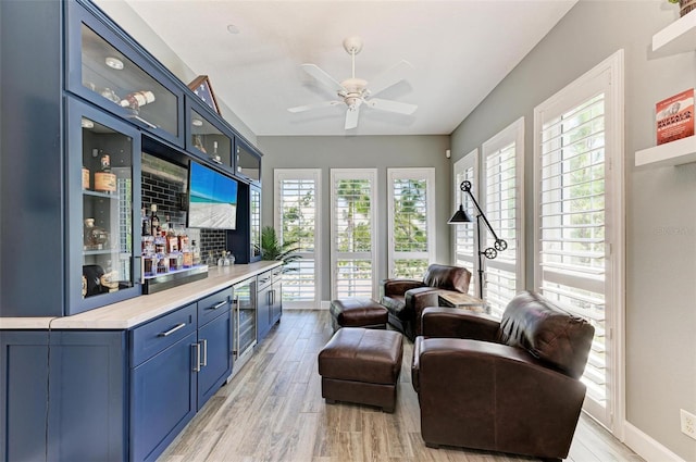 living room with bar area, wine cooler, ceiling fan, and light hardwood / wood-style floors