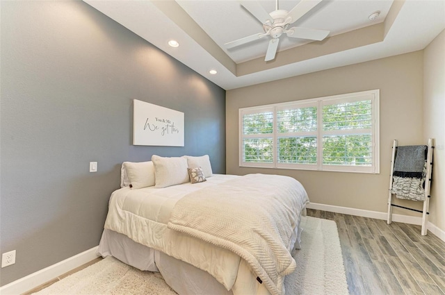 bedroom with hardwood / wood-style floors, ceiling fan, and a raised ceiling