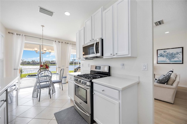 kitchen with appliances with stainless steel finishes, pendant lighting, white cabinets, and a chandelier