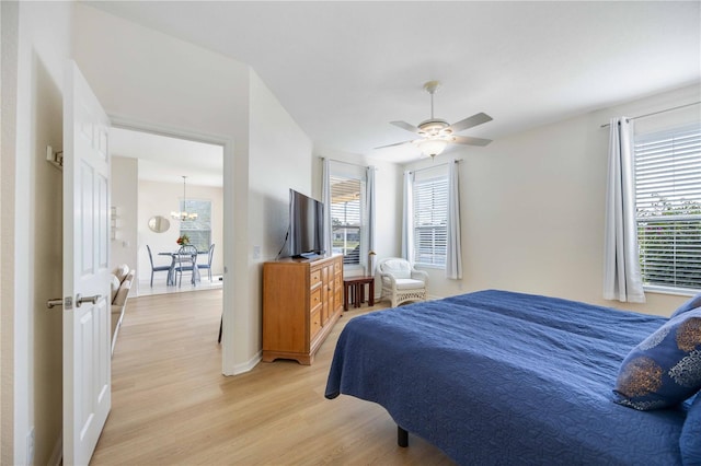 bedroom with ceiling fan with notable chandelier and light hardwood / wood-style flooring