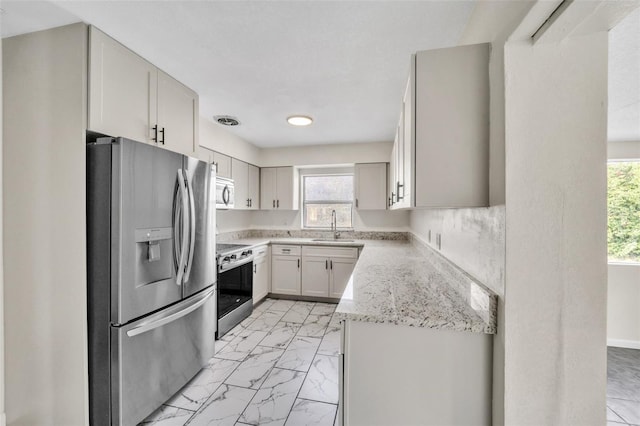 kitchen with appliances with stainless steel finishes, light stone counters, a wealth of natural light, sink, and white cabinets