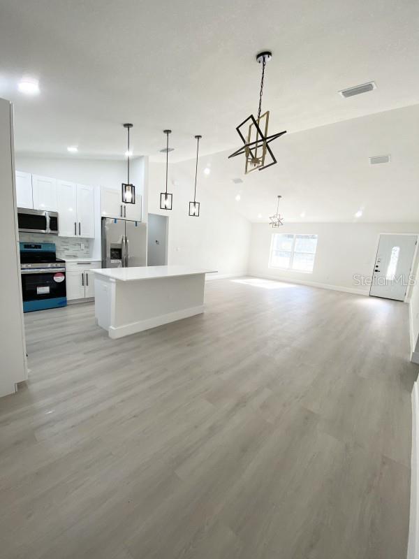 kitchen with a center island, backsplash, decorative light fixtures, white cabinetry, and stainless steel appliances