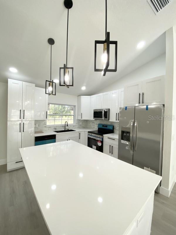 kitchen with white cabinets, a center island, stainless steel appliances, and hanging light fixtures