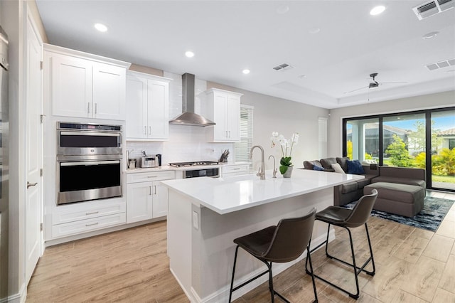 kitchen featuring appliances with stainless steel finishes, wall chimney exhaust hood, ceiling fan, white cabinets, and a breakfast bar area