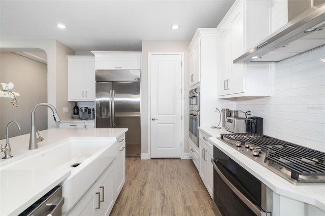 kitchen featuring sink, light hardwood / wood-style flooring, wall chimney exhaust hood, white cabinetry, and stainless steel appliances