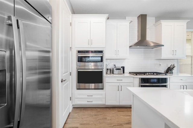 kitchen with white cabinets, appliances with stainless steel finishes, backsplash, and wall chimney exhaust hood