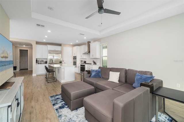 living room with a raised ceiling, light hardwood / wood-style flooring, and ceiling fan