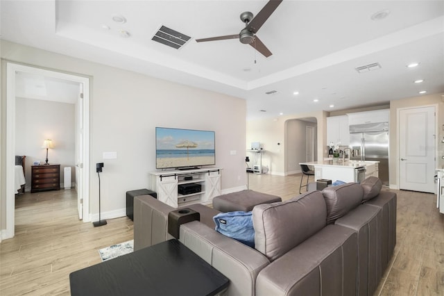 living room featuring ceiling fan, light hardwood / wood-style floors, and a raised ceiling