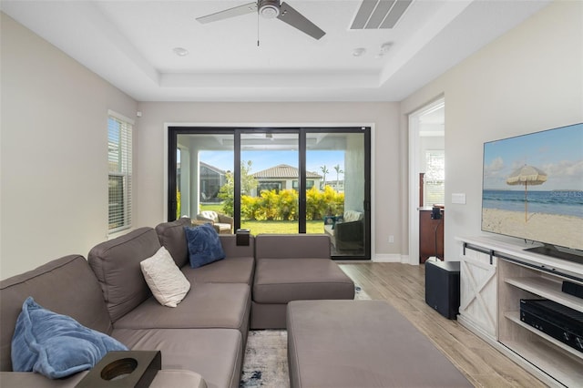 living room with a raised ceiling, ceiling fan, and light wood-type flooring