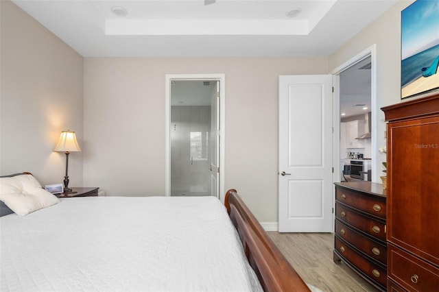 bedroom featuring ensuite bathroom, light hardwood / wood-style floors, and a tray ceiling