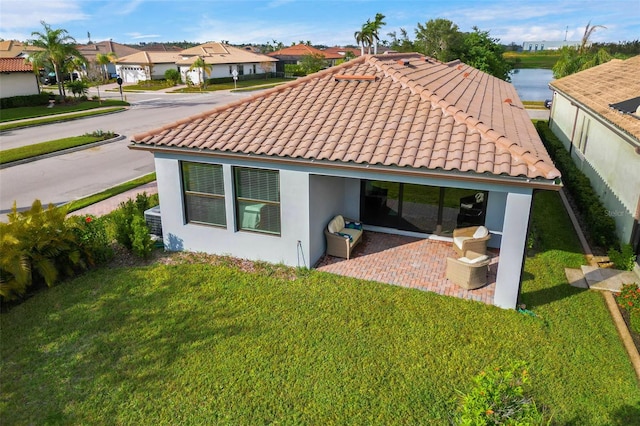 rear view of property featuring a water view, a patio area, and a lawn