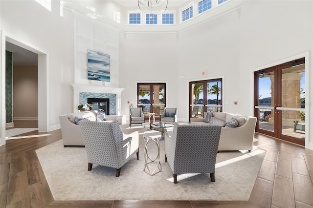 living room featuring french doors, a towering ceiling, hardwood / wood-style flooring, and a tiled fireplace