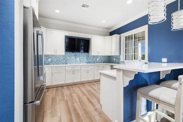 kitchen featuring white cabinets, a kitchen breakfast bar, hanging light fixtures, stainless steel fridge, and light hardwood / wood-style floors