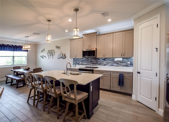 kitchen featuring pendant lighting, sink, appliances with stainless steel finishes, ornamental molding, and an island with sink