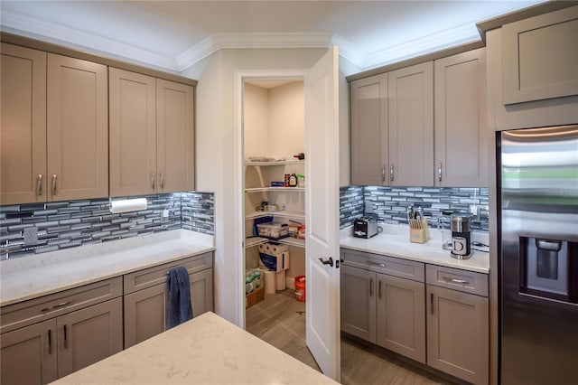 kitchen featuring crown molding, stainless steel fridge with ice dispenser, light hardwood / wood-style flooring, light stone countertops, and backsplash