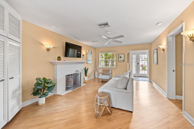 living room featuring light wood-type flooring, a brick fireplace, and ceiling fan