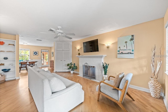 living room featuring ceiling fan, light hardwood / wood-style floors, and a brick fireplace