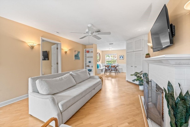 living room featuring a brick fireplace, ceiling fan, and light wood-type flooring