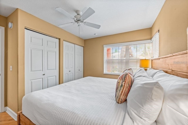 bedroom with ceiling fan, wood-type flooring, and multiple closets