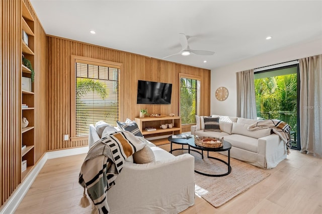 living room with wooden walls, ceiling fan, and light wood-type flooring