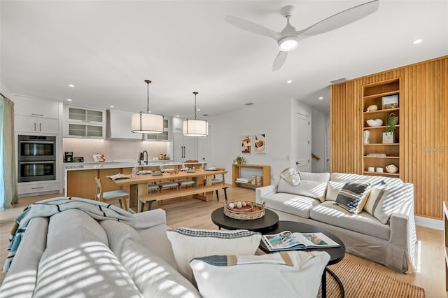 living room featuring ceiling fan, sink, and light wood-type flooring