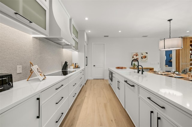 kitchen featuring white cabinets, black electric stovetop, sink, light wood-type flooring, and decorative light fixtures