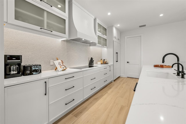 kitchen with black electric cooktop, light stone counters, sink, and white cabinets