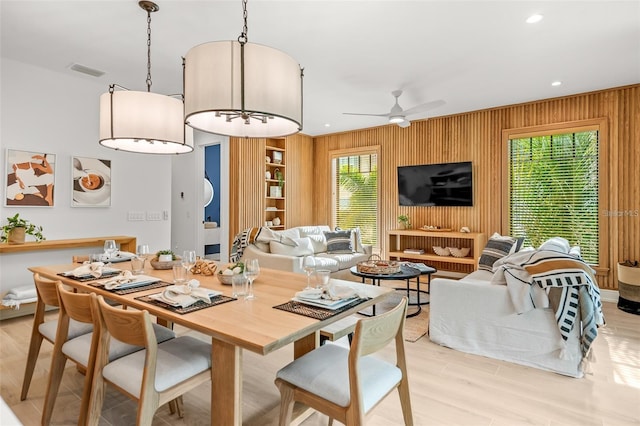 dining area featuring ceiling fan, light hardwood / wood-style floors, and wood walls