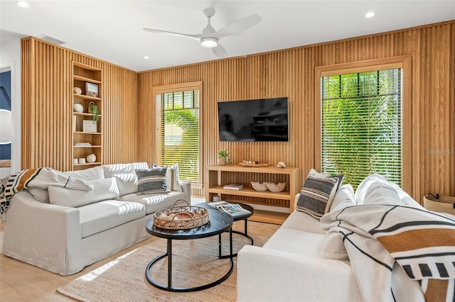 living room featuring ceiling fan, light hardwood / wood-style floors, and wood walls