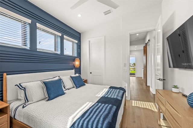 bedroom featuring a barn door, ceiling fan, light hardwood / wood-style flooring, and multiple windows