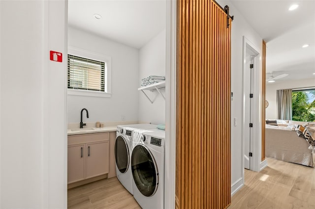 laundry room with sink, cabinets, a barn door, washer and clothes dryer, and light wood-type flooring