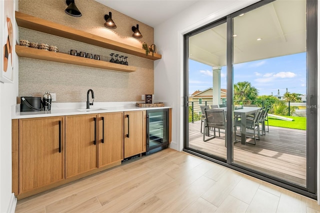 bar featuring decorative backsplash, light wood-type flooring, beverage cooler, and sink