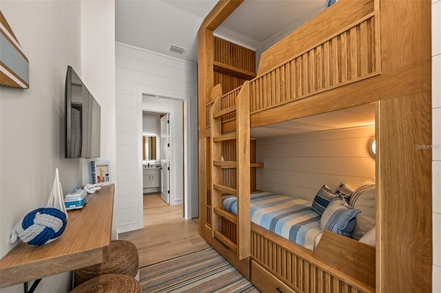 bedroom with wood walls, light hardwood / wood-style floors, and ensuite bath