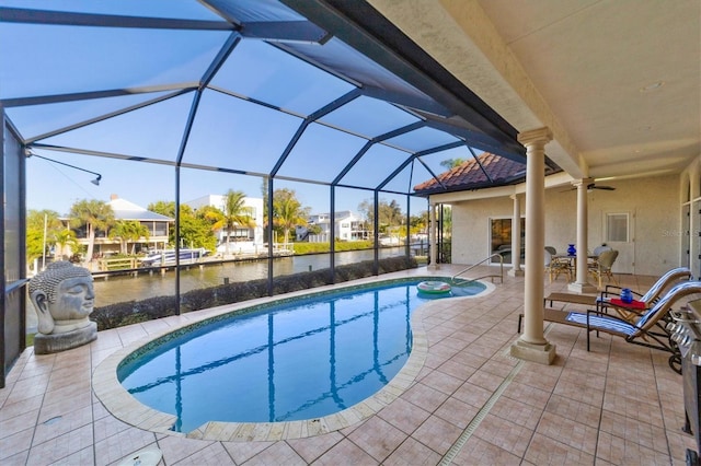 view of pool with glass enclosure, ceiling fan, a water view, and a patio area