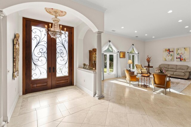 tiled foyer featuring ornate columns, french doors, a notable chandelier, and ornamental molding